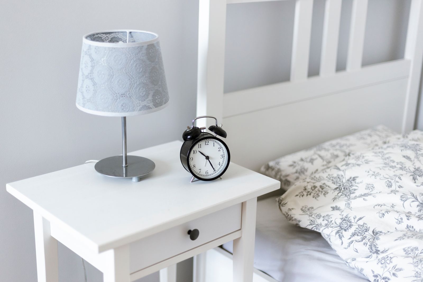 A calm bedroom with a small clock and lamp on a bedside table.