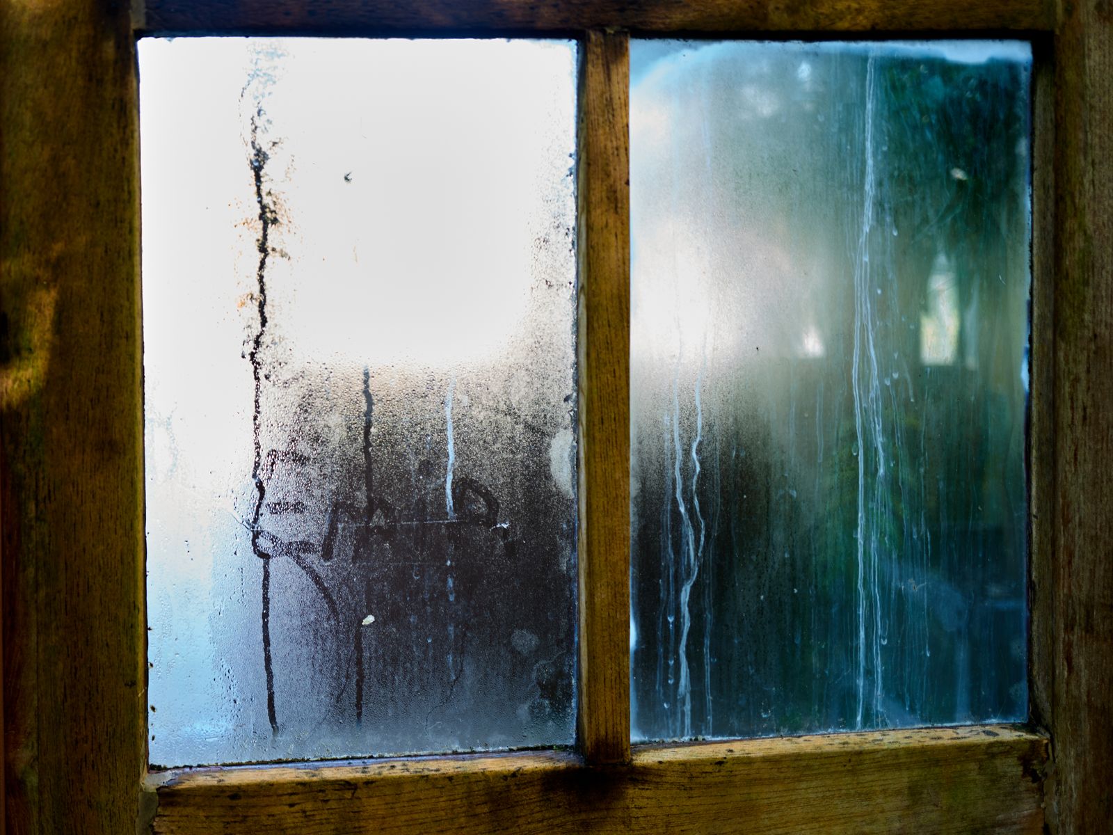 Condensation and water droplets on the glass of a wooden-framed home window.