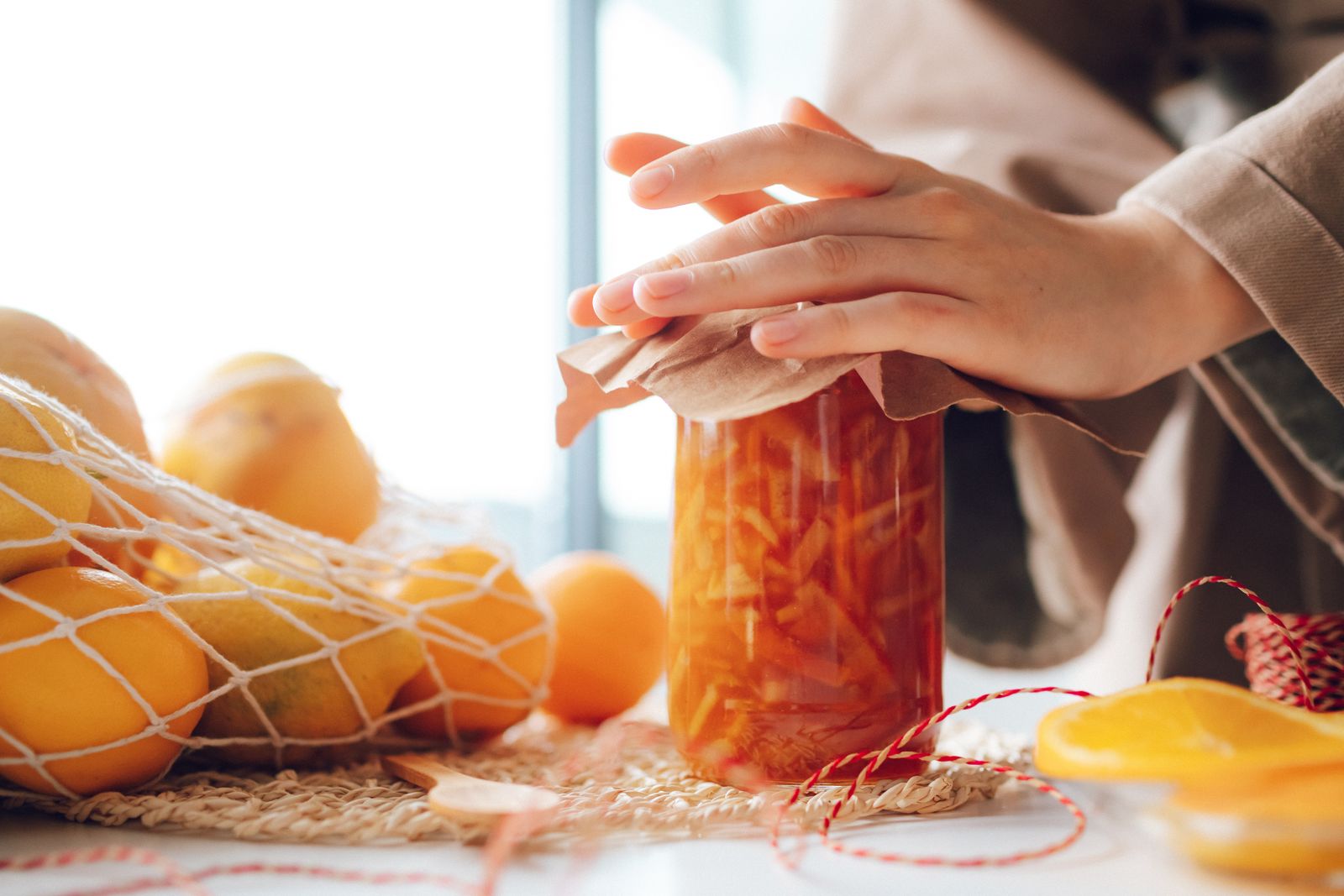 Hands filling a glass jar with orange marmalade on a kitchen worktop.