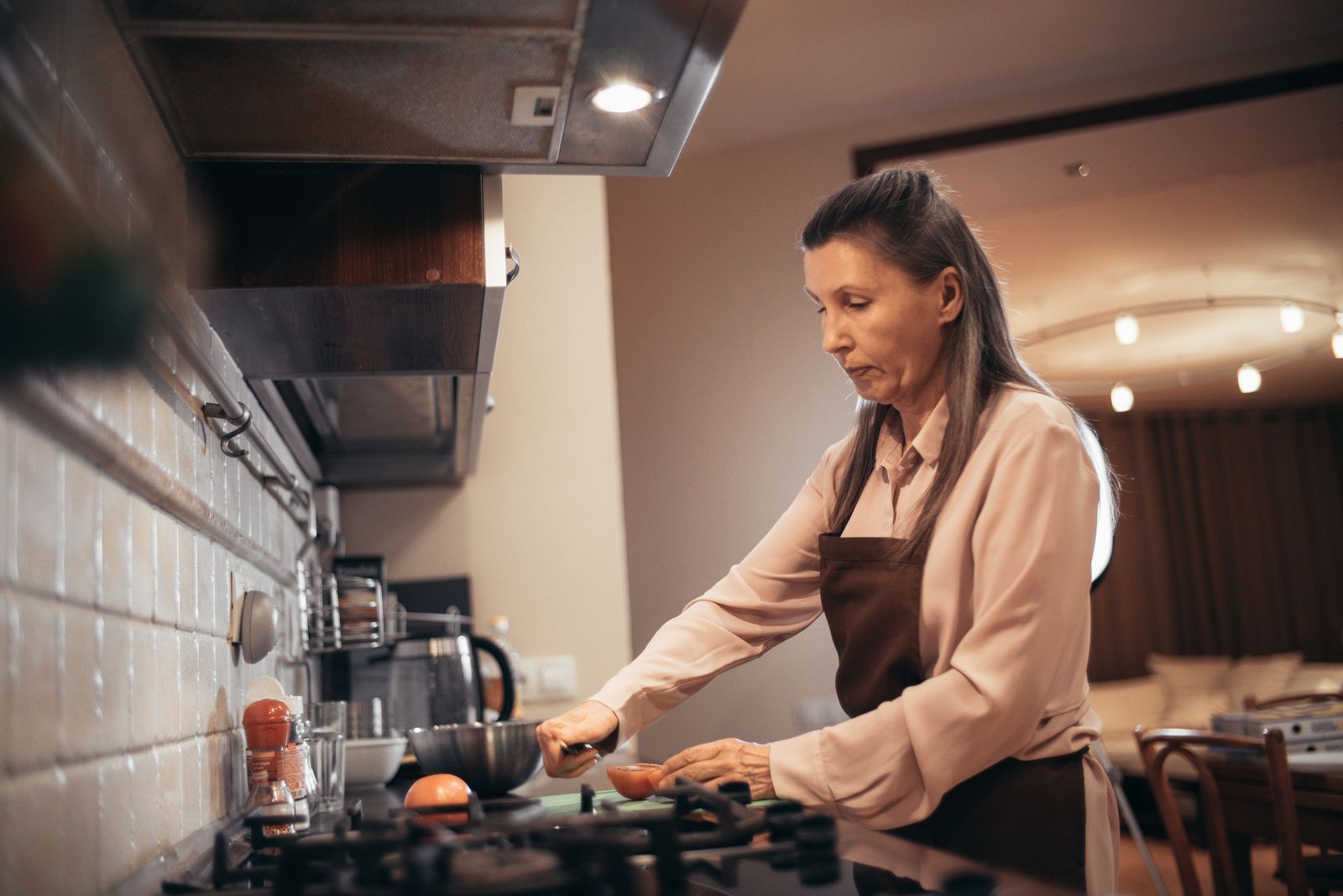 An older woman preparing food in a warm home kitchen.