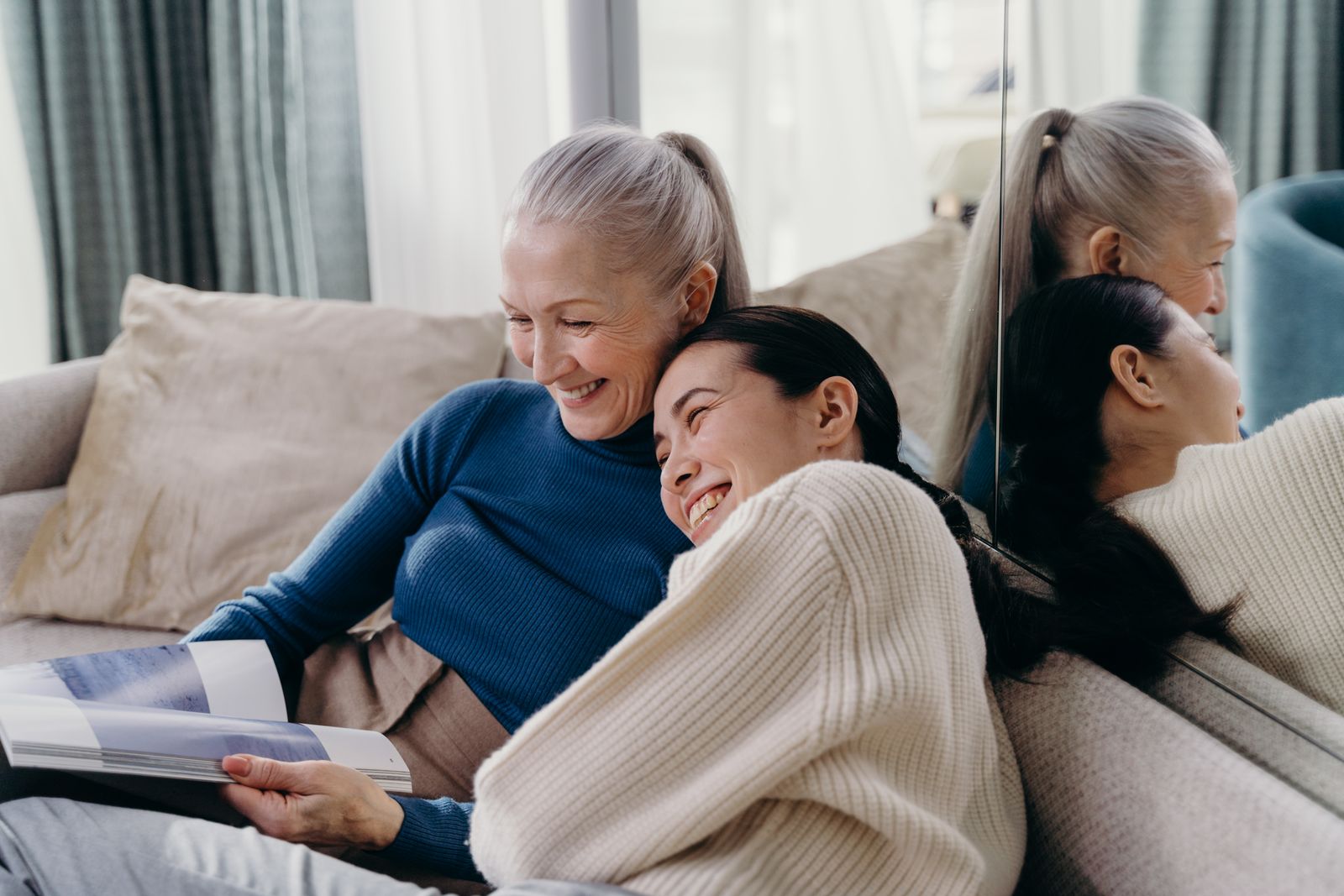 An older woman and a younger woman laughing together on a sofa at home.
