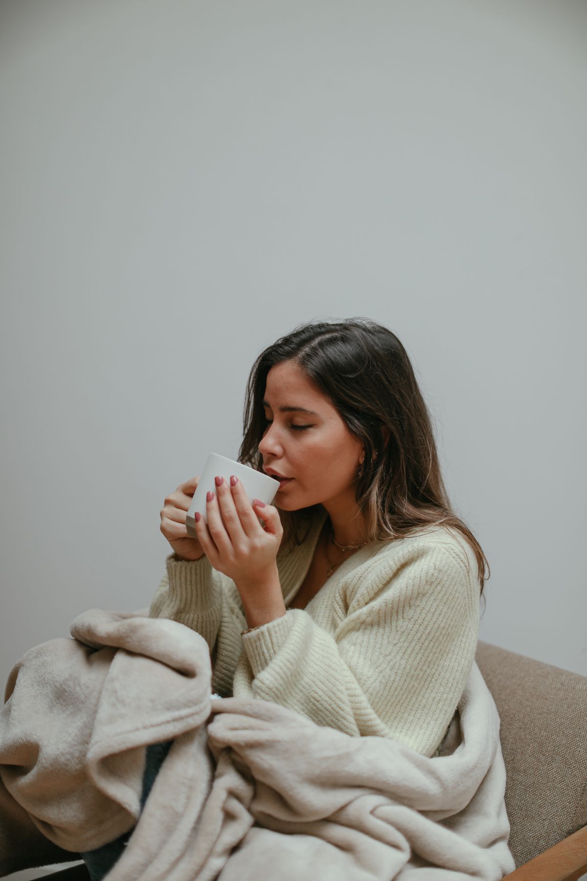 A woman wrapped in a blanket relaxing with a hot cup of tea.