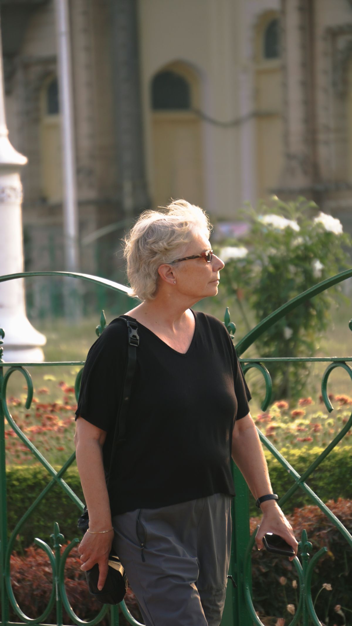 An older woman with grey hair and glasses walking confidently through a park.